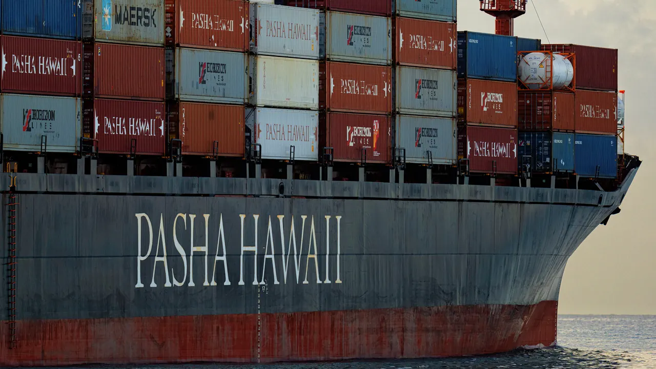 Container ship departing Honolulu Harbor with stacked shipping containers on deck